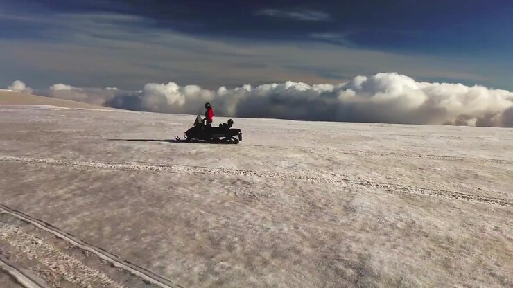 Aerial landscape view of a person riding a snowmobile on the surface of a glacier in Iceland, over the clouds, on a sunny day