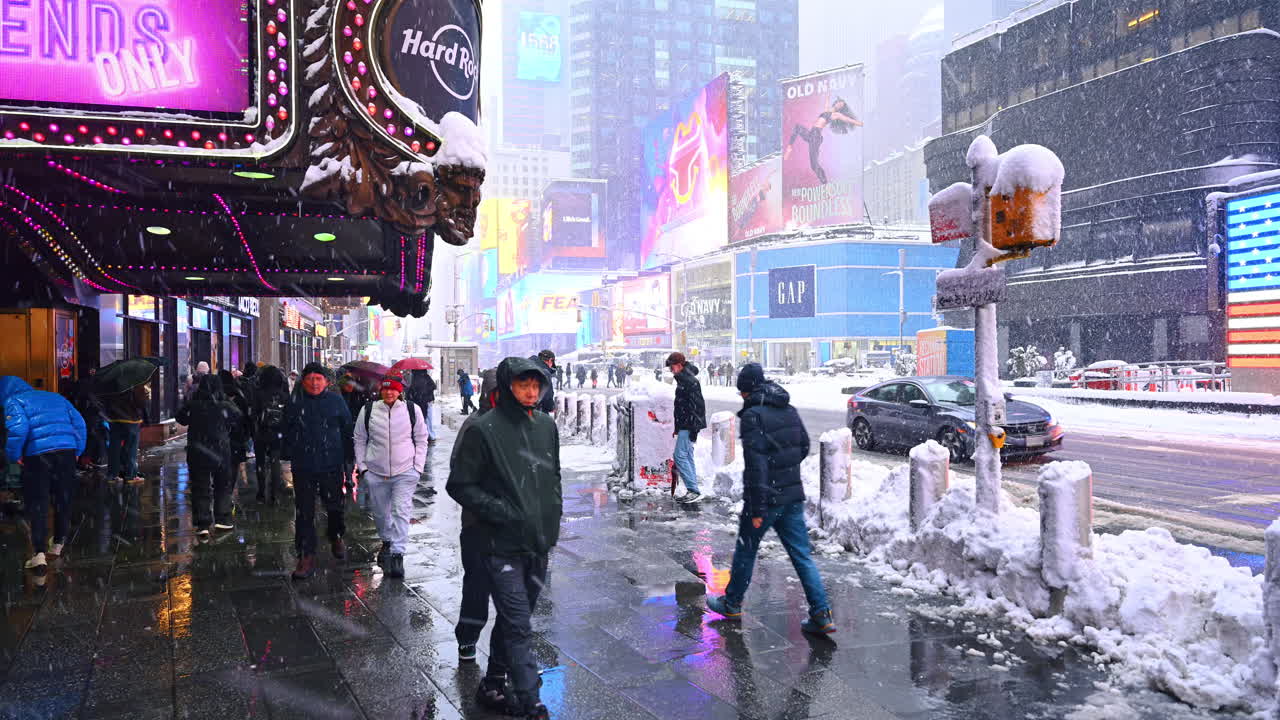 New York, USA, 22. februar 2026: Fodgængere går på glat fortov under kraftigt snefald. Folk i vintertøj navigerer på våd og snefyldt gade forbi neonskilte under Manhattans vinterstorm.