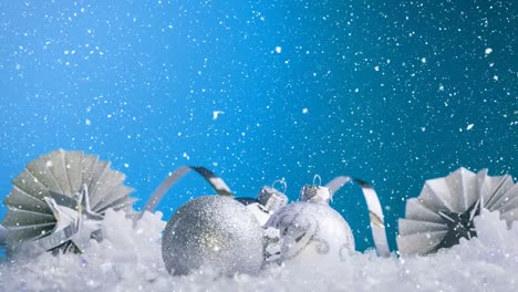 Animation-of-snow-falling-over-white-and-silver-christmas-decorations-on-blue-background