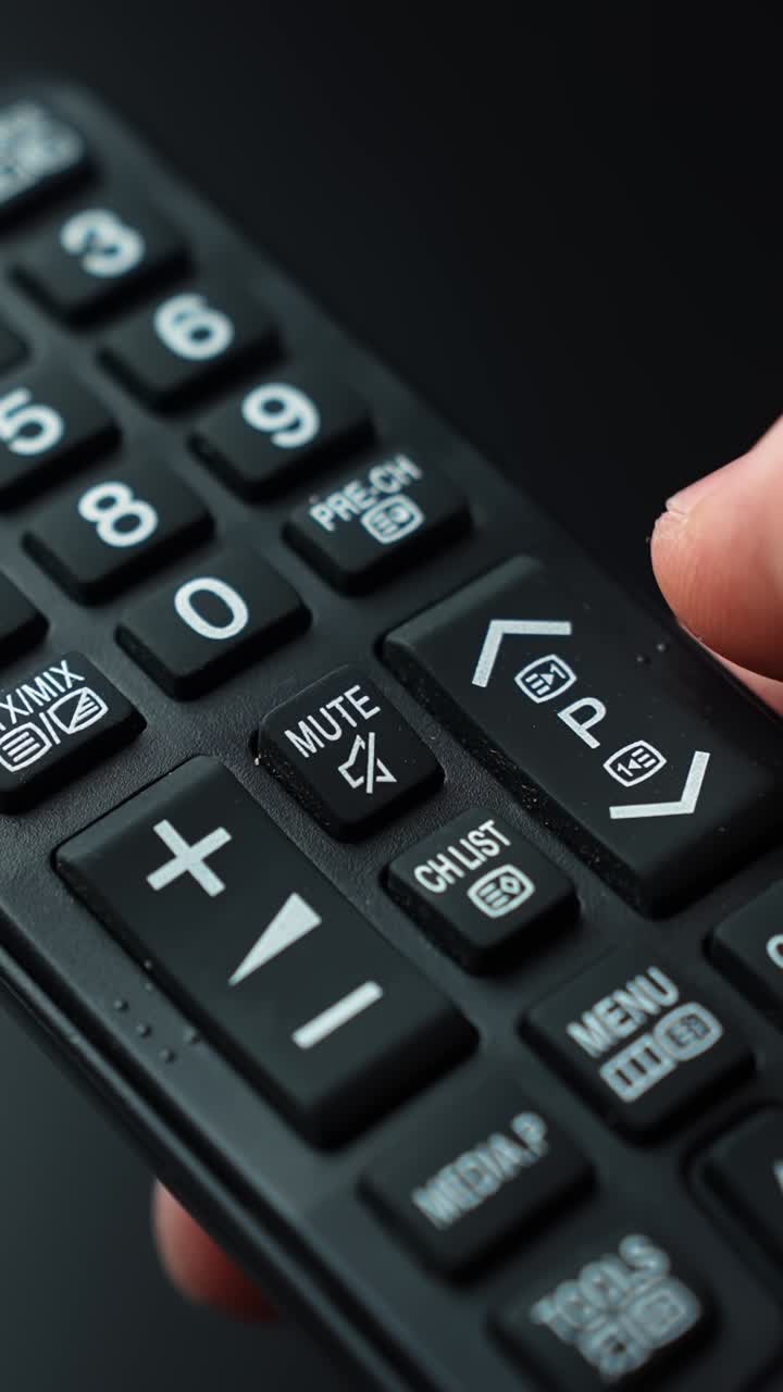 Scatto macro verticale di una mano che preme il pulsante muto su un telecomando della TV, mostrando il controllo audio e l'attivazione/disattivazione rapida del suono in una moderna configurazione di intrattenimento domestico.