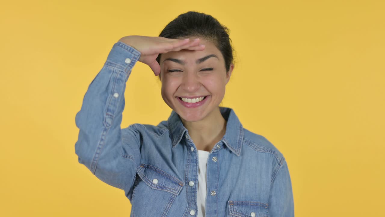 젊은 인도 여성은 주위를 둘러보고, 노란색 배경을 찾고 있습니다.