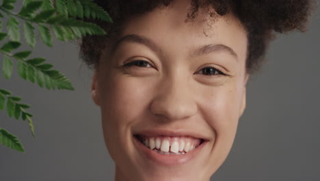 retrato de cerca hermosa mujer de raza mixta tocando el rostro con una hoja acariciando la piel suave y saludable disfrutando de la belleza natural juguetona sobre un fondo gris