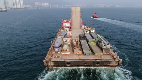 barge loaded with concrete mixer trucks pulled to port by a tugboat in hong kong bay, aerial view