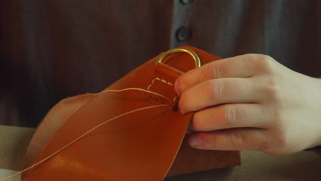 a professional tailor tanner sews an accessory attachment to a bag made of genuine leather. close-up, slow motion