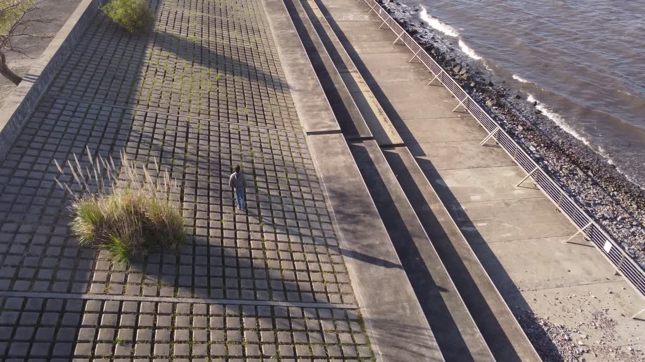 Um jovem caminhando pela orla de Buenos Aires sobre as pedras quadradas da margem