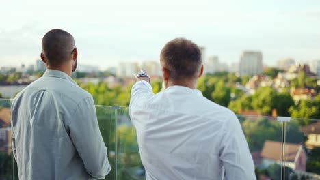 Two-happy-businessmen-chatting-on-a-terrace-overlooking-the-city.-Beautiful-view.-communication