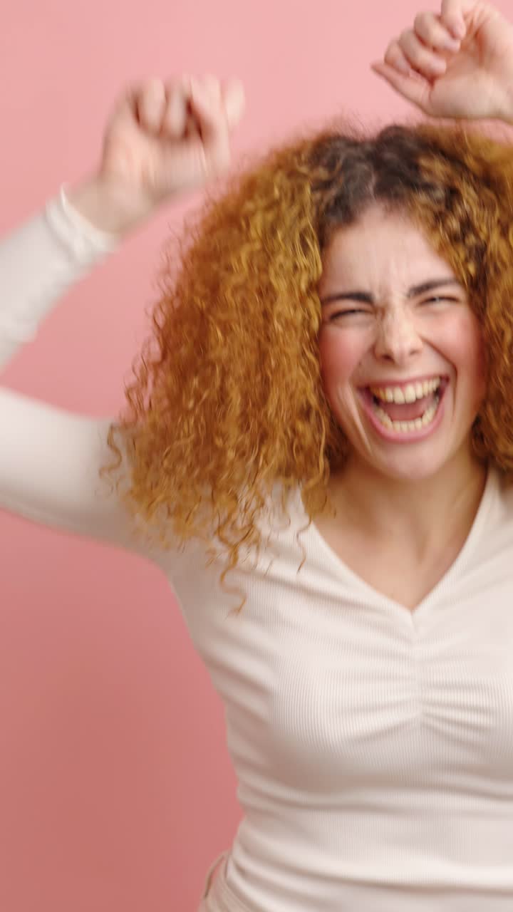 Enthusiastic young woman celebrating with arms raised on pink background