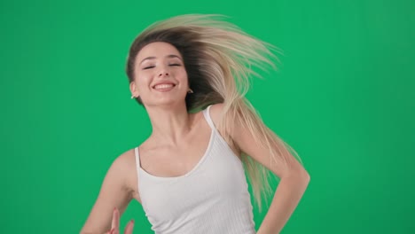 portrait of beautiful dancing blonde girl with long hair performs a dance movement on green background, look into camera, chrome key