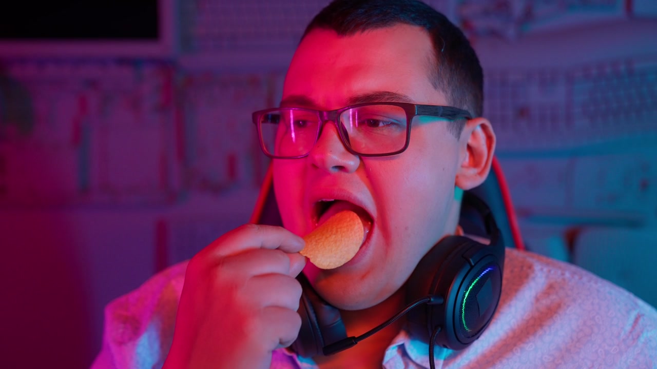 Giovane uomo che mangia patatine in una stanza illuminata al neon