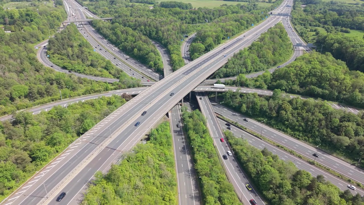 Pemandangan udara sistem jalan raya yang kompleks. Mobil dan truk melaju di banyak jalan dan jembatan. Persimpangan itu dikelilingi oleh hutan hijau lebat. Ini adalah hari yang cerah di musim semi atau musim panas