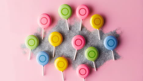 a vibrant arrangement of colorful lollipops on a pink, glittery background