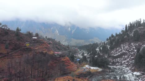 Rückwärtsfliegende-Luftaufnahme-Einer-Alten-Stadt-In-Manali-Mit-Starkem-Schneefall-In-Der-Nähe-Des-Manalsu-Flussufers-In-Himachal-Pradesh,-Aufgenommen-Mit-Einer-Drohne-In-4K