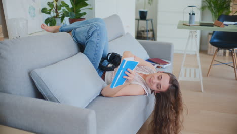 woman lays upside down on sofa reading book