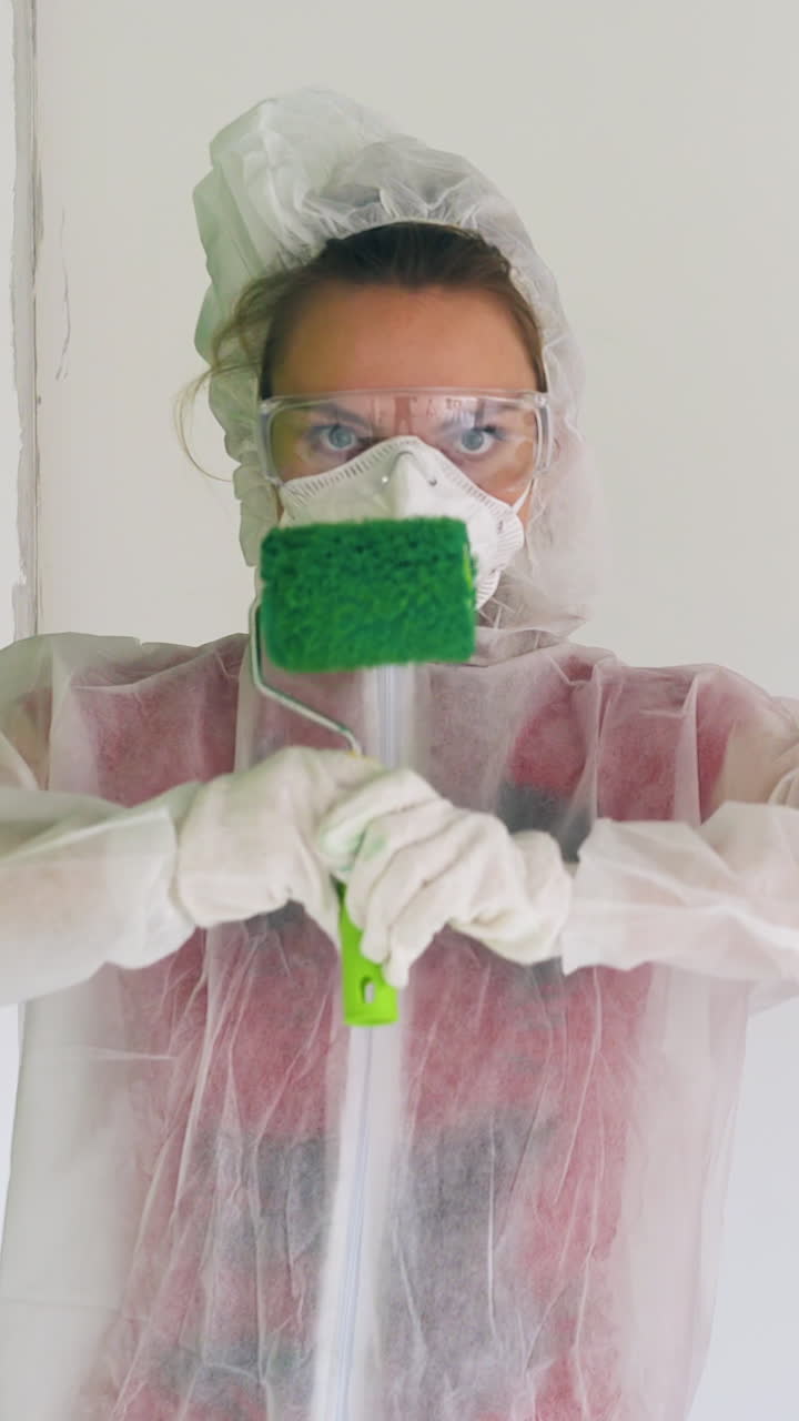 young couple wearing protective workwear with hoods and respirators poses holding rollers in green paint at construction