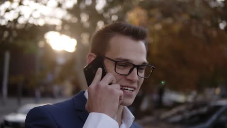 portrait of businessman in stylish glasses talking on the mobile phone on streets of business district. young smiling man using