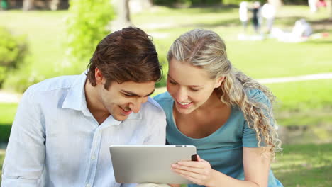 a smiling couple use a tablet pc in the park as they look at the camera at the end