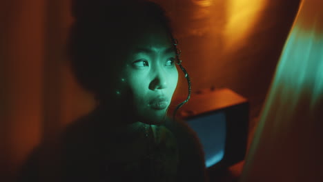 young asian woman looking up in dark studio with neon light and old tv