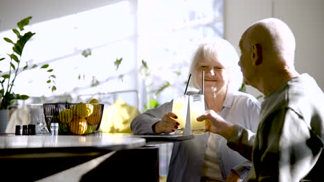 senior couple drinking limonade and toasting while they are sitting in a bar at sunset