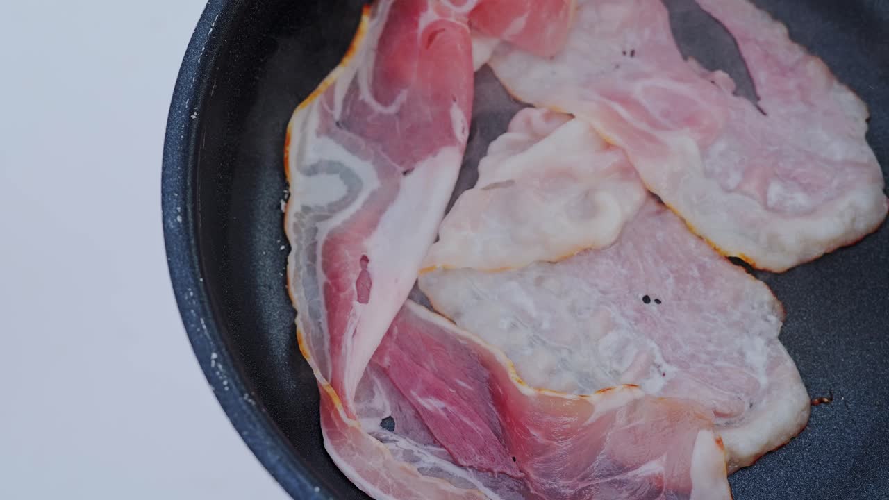 Strips of raw bacon begin to sizzle in hot pan atop picnic camp table