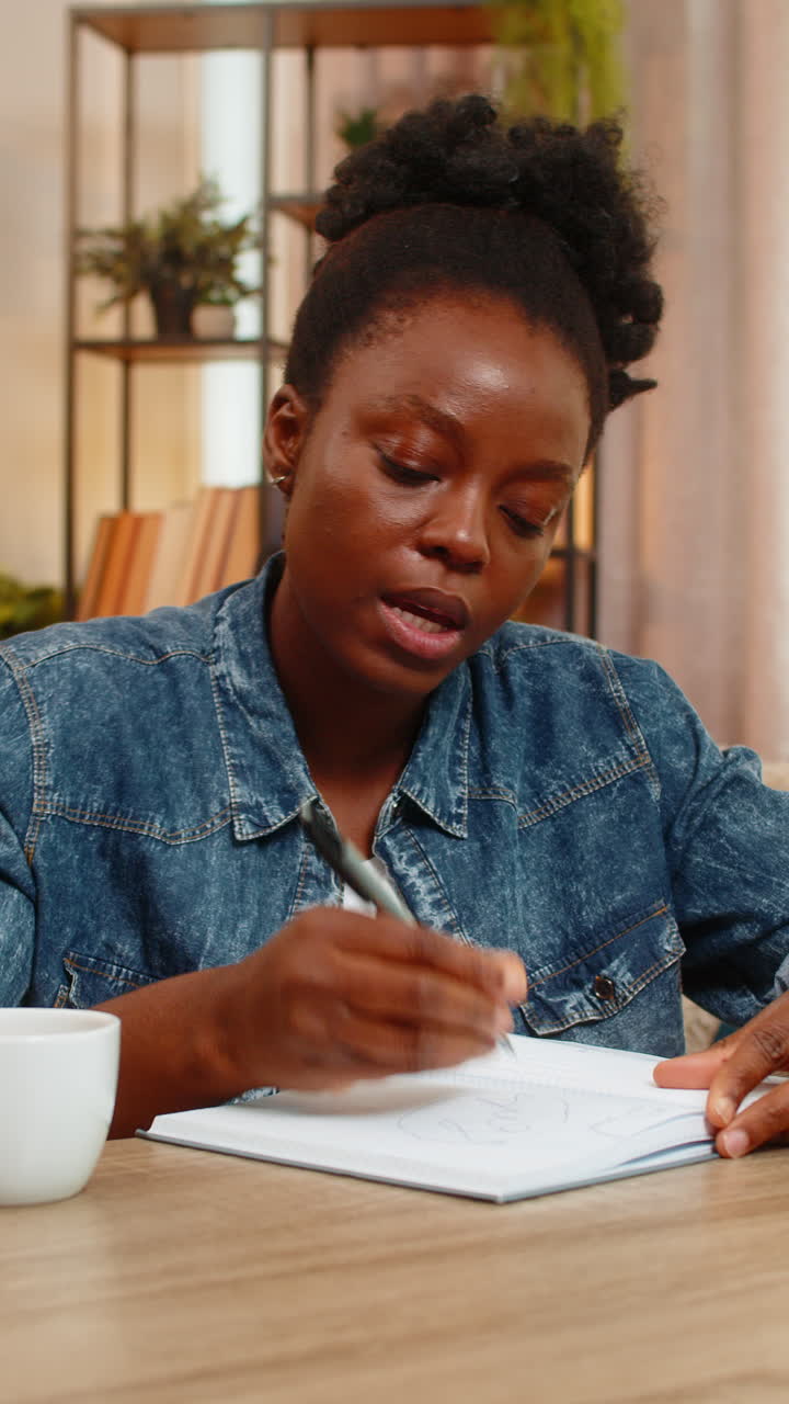 Giovane donna afroamericana freelance che crea uno schizzo di logo su un quaderno al tavolo di casa.