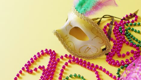 video of masquerade mask with feathers and mardi gras beads on yellow background with copy space