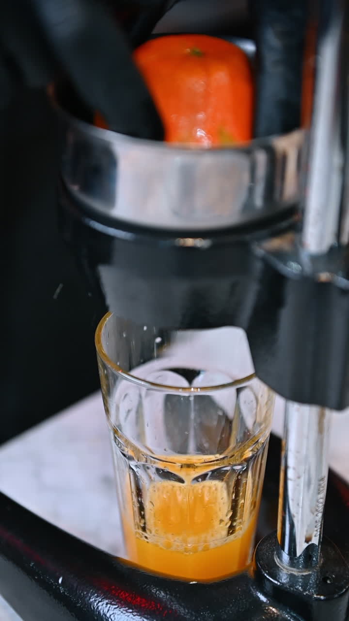 Succo d'arancia appena spremuto in un bicchiere. Primo piano di uno spremiagrumi in metallo che versa succo d'arancia fresco in un bicchiere trasparente