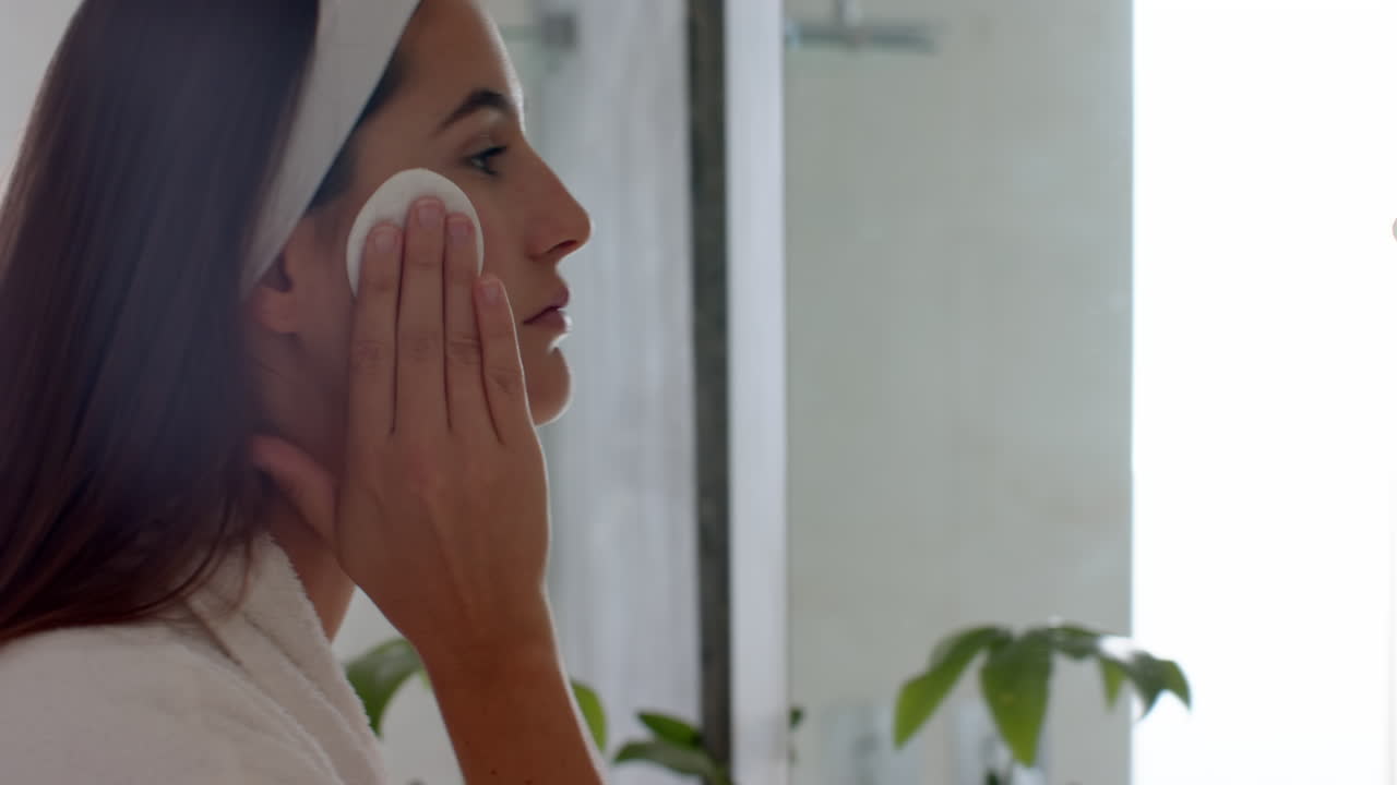 Applying facial cleanser, woman in bathrobe enjoying skincare routine at home