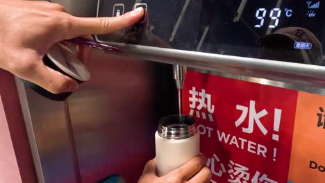 person filling a cup with hot water from dispenser