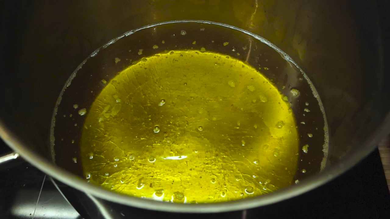 Primo piano di olio giallo dorato per friggitrice che bolle ad alta temperatura in una pentola grigio acciaio su un fornello di casa. L'olio è molto caldo e si riflette sui lati della pentola d'acciaio.