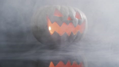 Smoke-effect-over-scary-face-carved-halloween-pumpkin-against-grey-background
