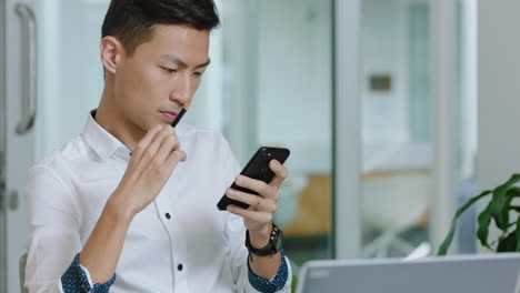 young asian businessman using smartphone texting checking messages on mobile phone contemplating sending email communication browsing online at work in office