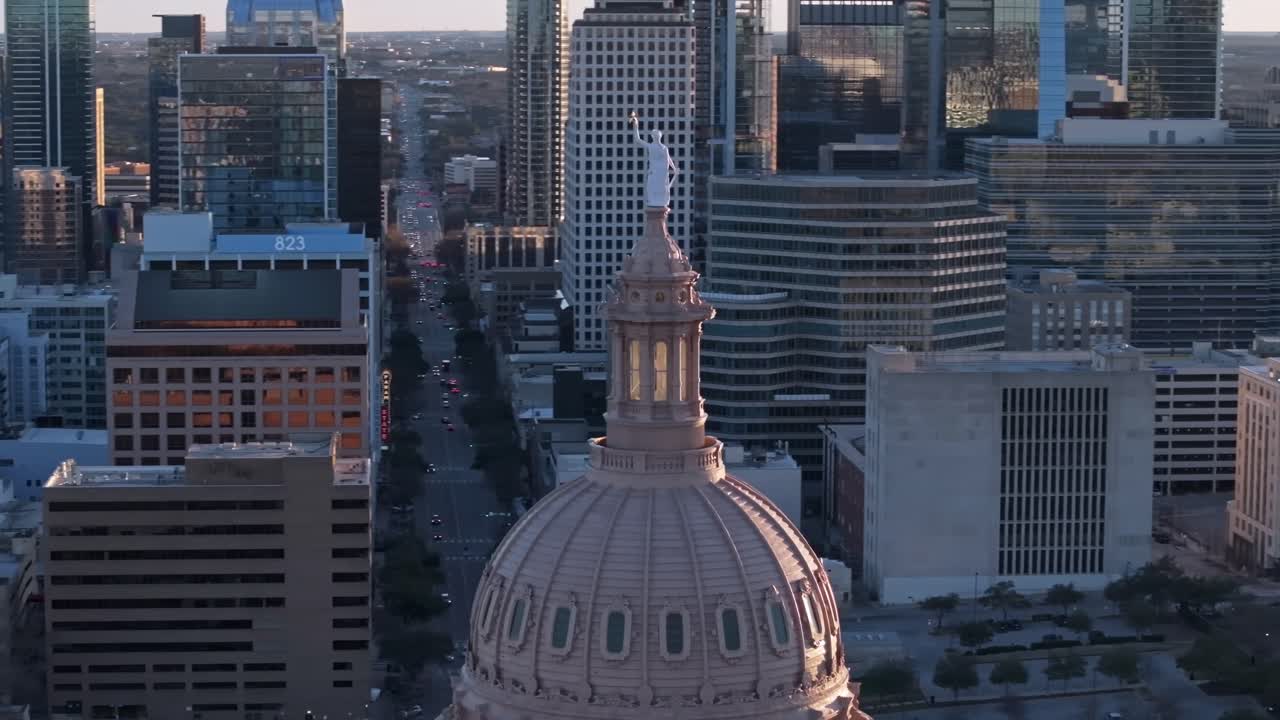 A zoomed-in drone shot with parallax circling the Texas State Capitol building in Austin Texas with Congress Ave. in the background with the sunset backlighting the Goddess of Liberty statue on top