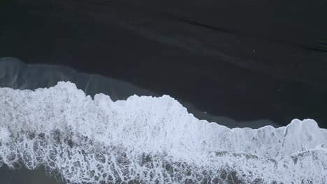 waves crash onto a surf beach with black sand