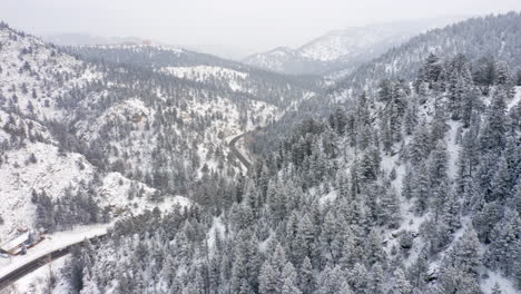 aerial reveal left of boulder canyon drive in colorado during the winter as cars drive down icy road surrounded by rocky mountains and snow covered pine trees