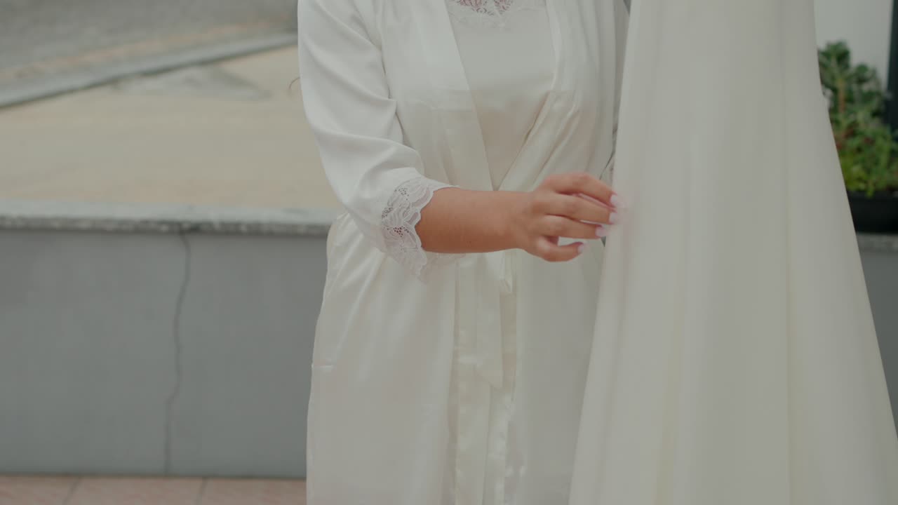 Bride in a white robe gently holding her wedding dress, preparing for the ceremony