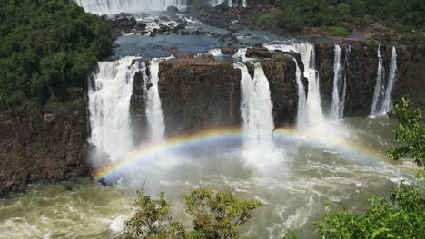 Hermosos-Colores-Del-Arco-Iris-Formados-Por-Salpicaduras-De-Cascada-En-Las-Cataratas-Del-Iguazú,-Brasil,-Vista-En-ángulo-Alto-Del-Hermoso-Borde-Del-Acantilado-Y-Cascadas-Rugosas-Que-Miran-Sobre-El-Colorido-Y-Brillante-Arco-Del-Arco-Iris