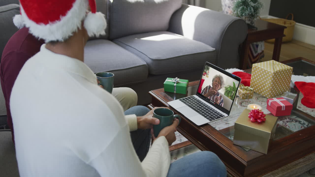 padre y hijo biraciales usando una computadora portátil para una videollamada de navidad con una mujer sonriente en la pantalla