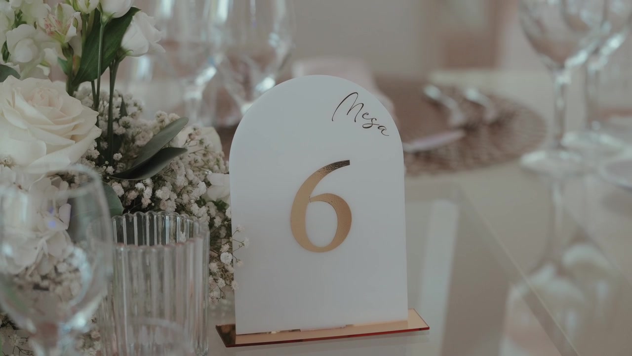 Segnaposto da tavolo numero sei dorato tra rose bianche e calici di champagne a un ricevimento di matrimonio.