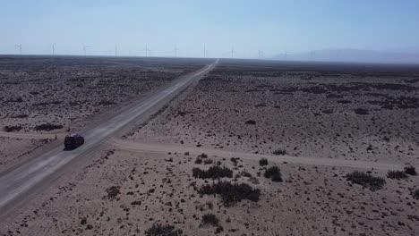 Das-Drohnenbild-Zeigt-Ein-Auto-Auf-Einer-Verlassenen-Straße-Auf-Dem-Weg-Zu-Einem-Windpark