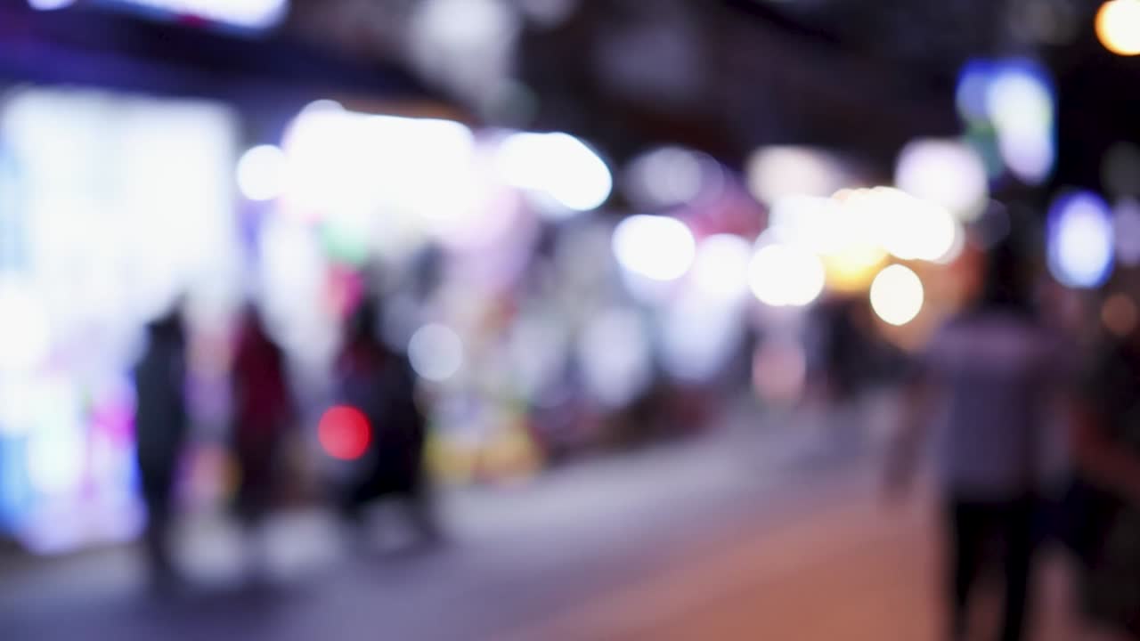 Vista sfocata di strada notturna con luci bokeh colorate e silhouette di turisti che camminano