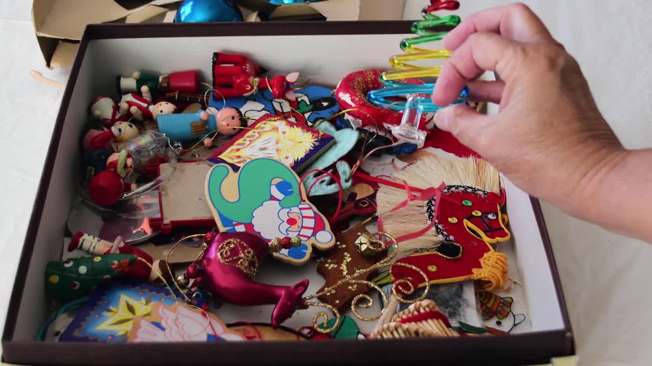 한 손이 크리스마스 트리 장식 상자의 모서리에 닿아 무시하는 것보다 검사를 위해 하나를 들어 올립니다.