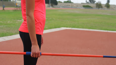 Side-view-of-Caucasian-female-athlete-holding-javelin-stick-and-standing-at-sports-venue-4k