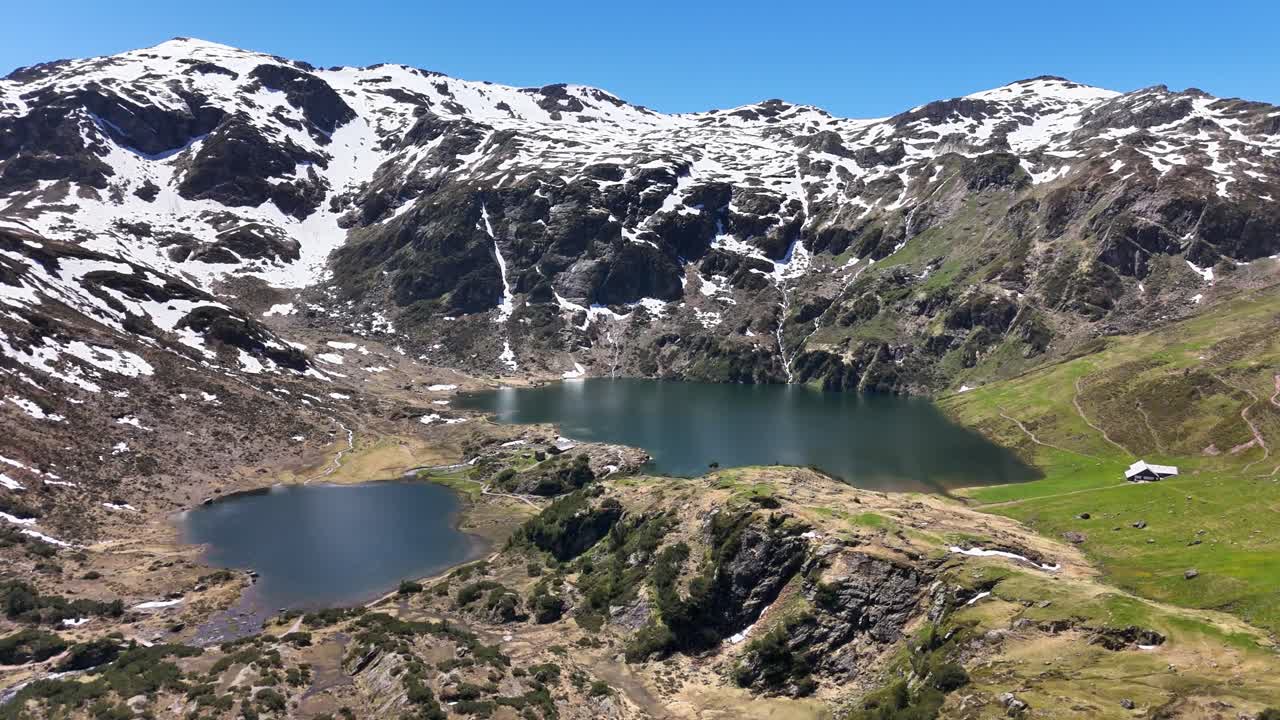 Murgsee in Switzerland features alpine lakes surrounded by snow covered peaks, rugged terrain, and green meadows, with mountain cabins visible, under a bright blue sky in a pristine natural landscape