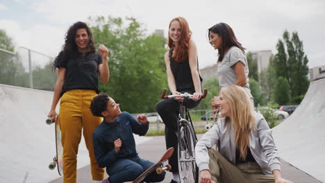 portrait of female friends with skateboards and bike standing in urban skate park