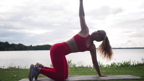 young woman in red sportswear sitting on yoga mat outside doing exercises and practicing yoga