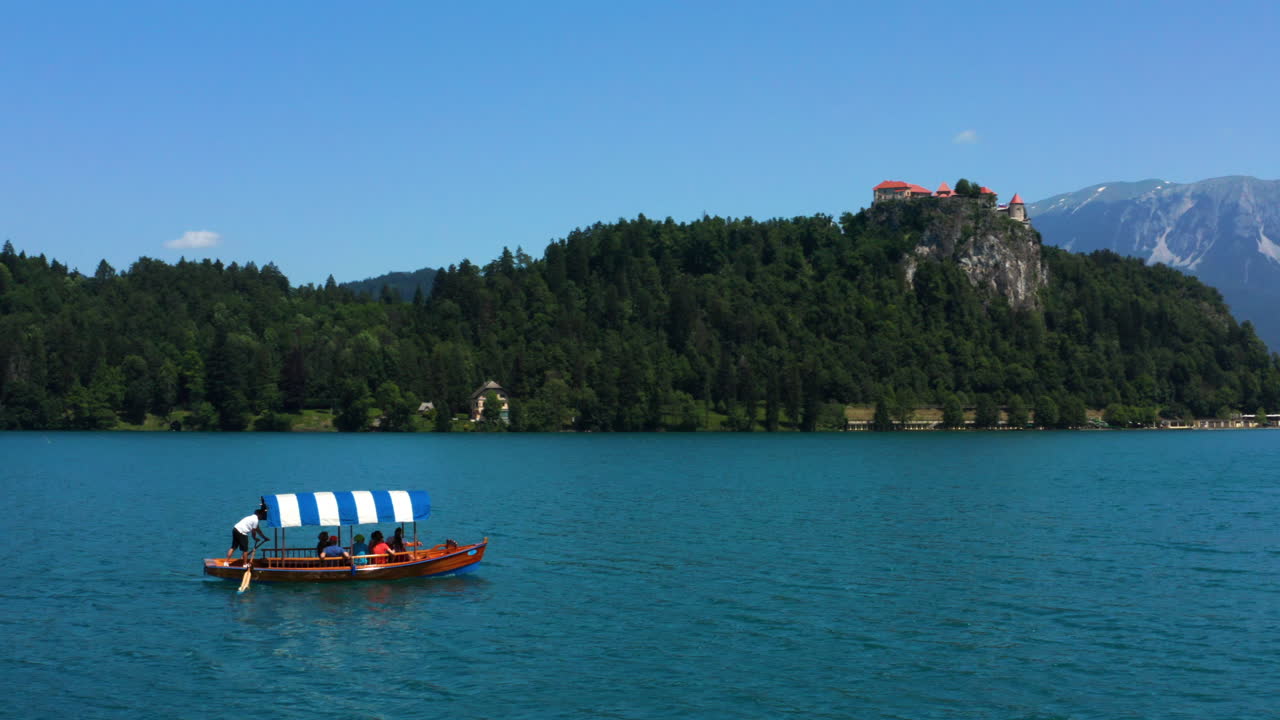 Turisti in crociera su una barca Pletna sul Lago di Bled, con vista sulla Chiesa del Pellegrinaggio e sul castello in cima alla collina in Slovenia.