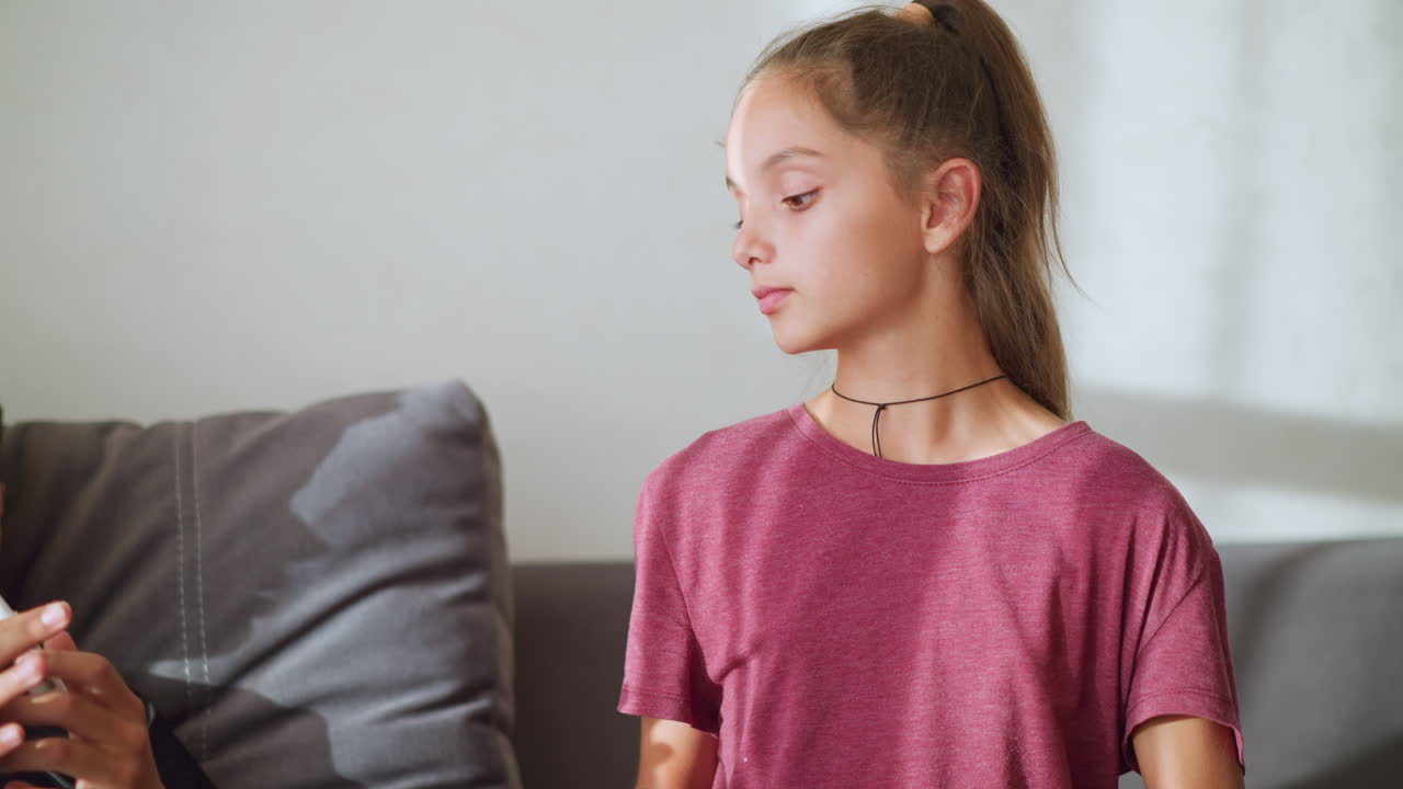 Caring sister hands over thermometer to sick brother to check his temperature, he is resting on the couch under a warm blanket, demonstrating sibling love and concern