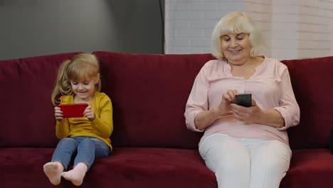 Senior-grandmother-with-child-girl-granddaughter-using-digital-mobile-phone,-playing-games-at-home