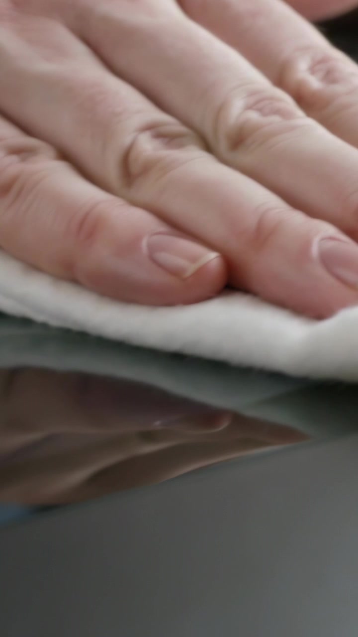 Vertical video: Seeing dust, hand pressing and wiping folded white cloth at desk, revealing clarity