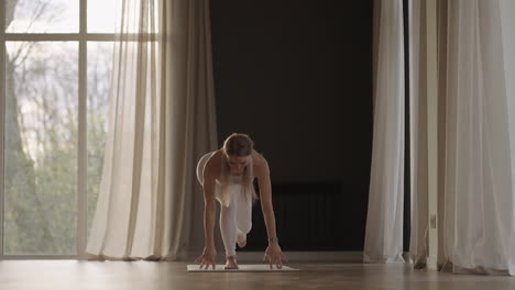 a young woman in a white suit in a gym trains yoga in the sun in slow motion